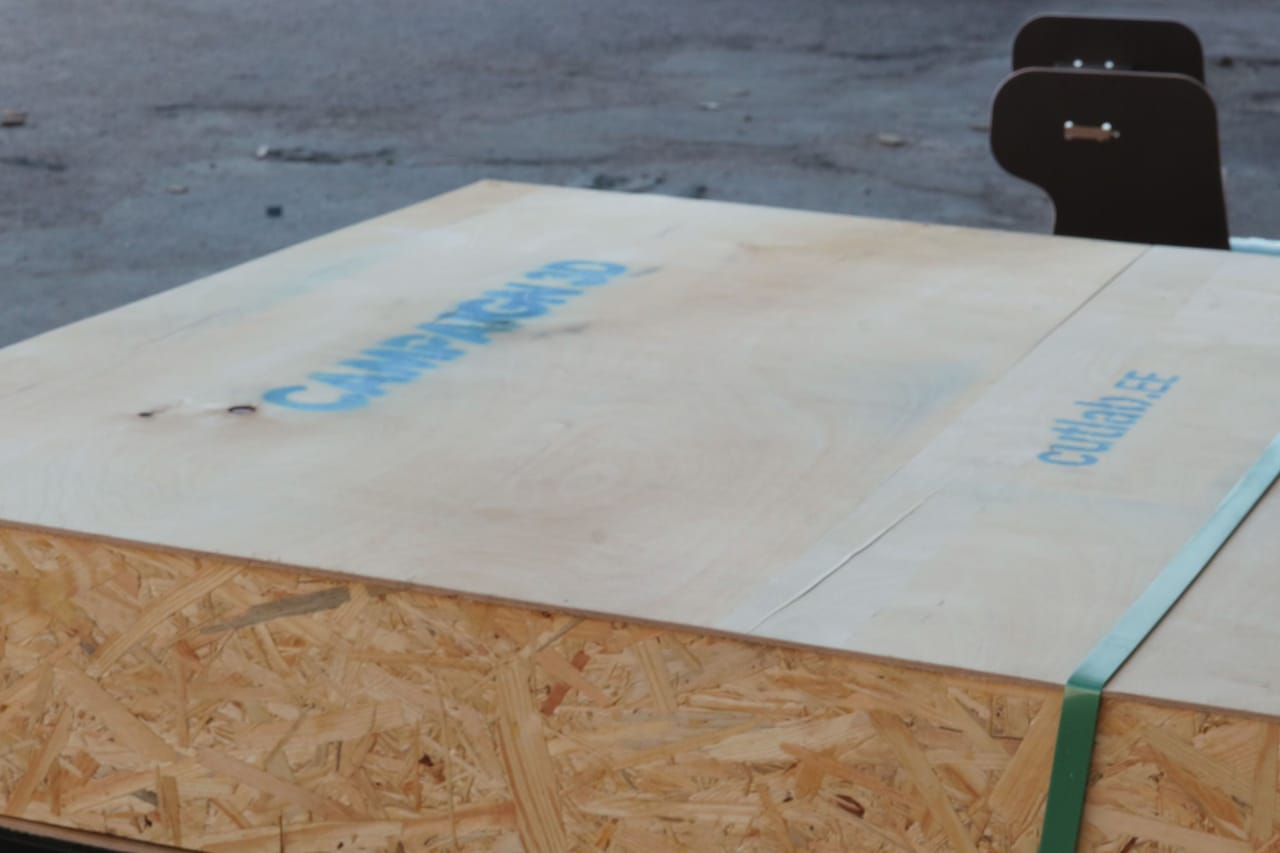 Corner of a plywood and OSB crate with a stencilled lid and green strapping
