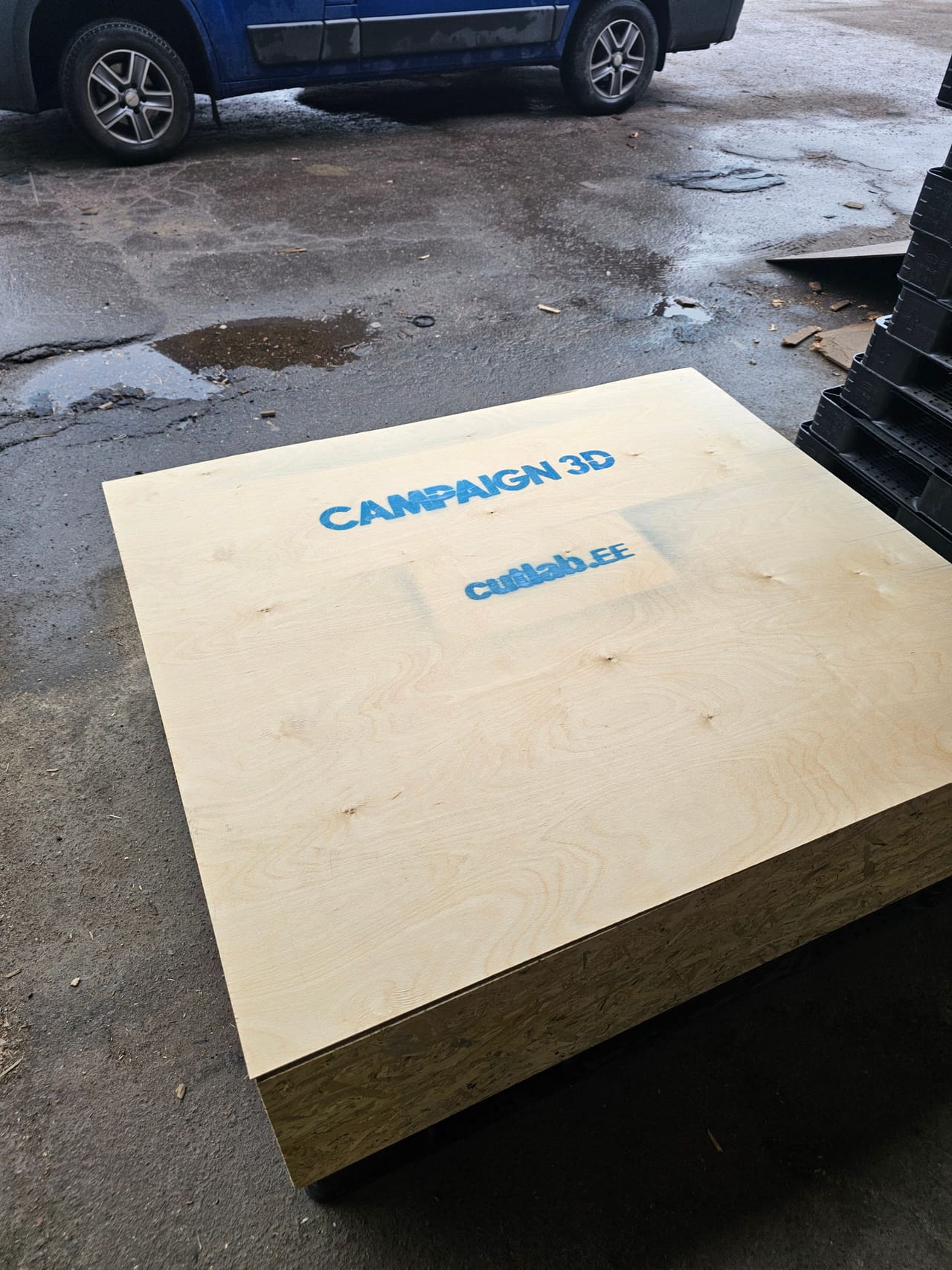 Plywood crate lid with a stencil, OSB edge visible, photographed outdoors