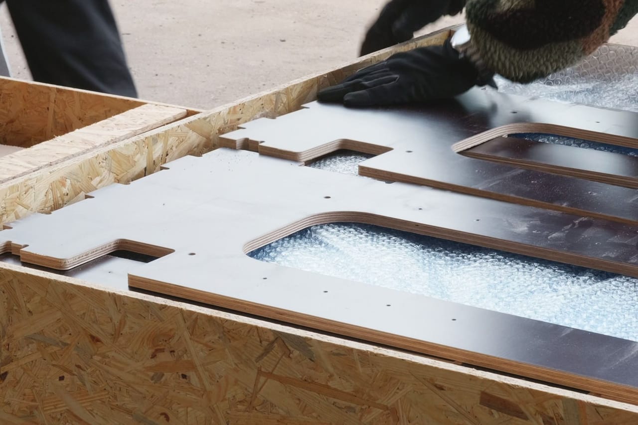 Birch plywood parts with CNC-cut slots lying on bubble wrap inside an OSB crate