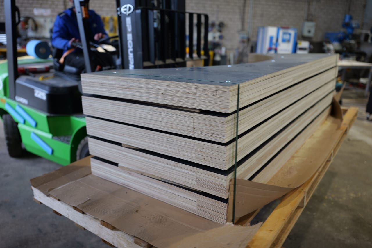 Stack of curved plywood parts on a pallet, forklift behind