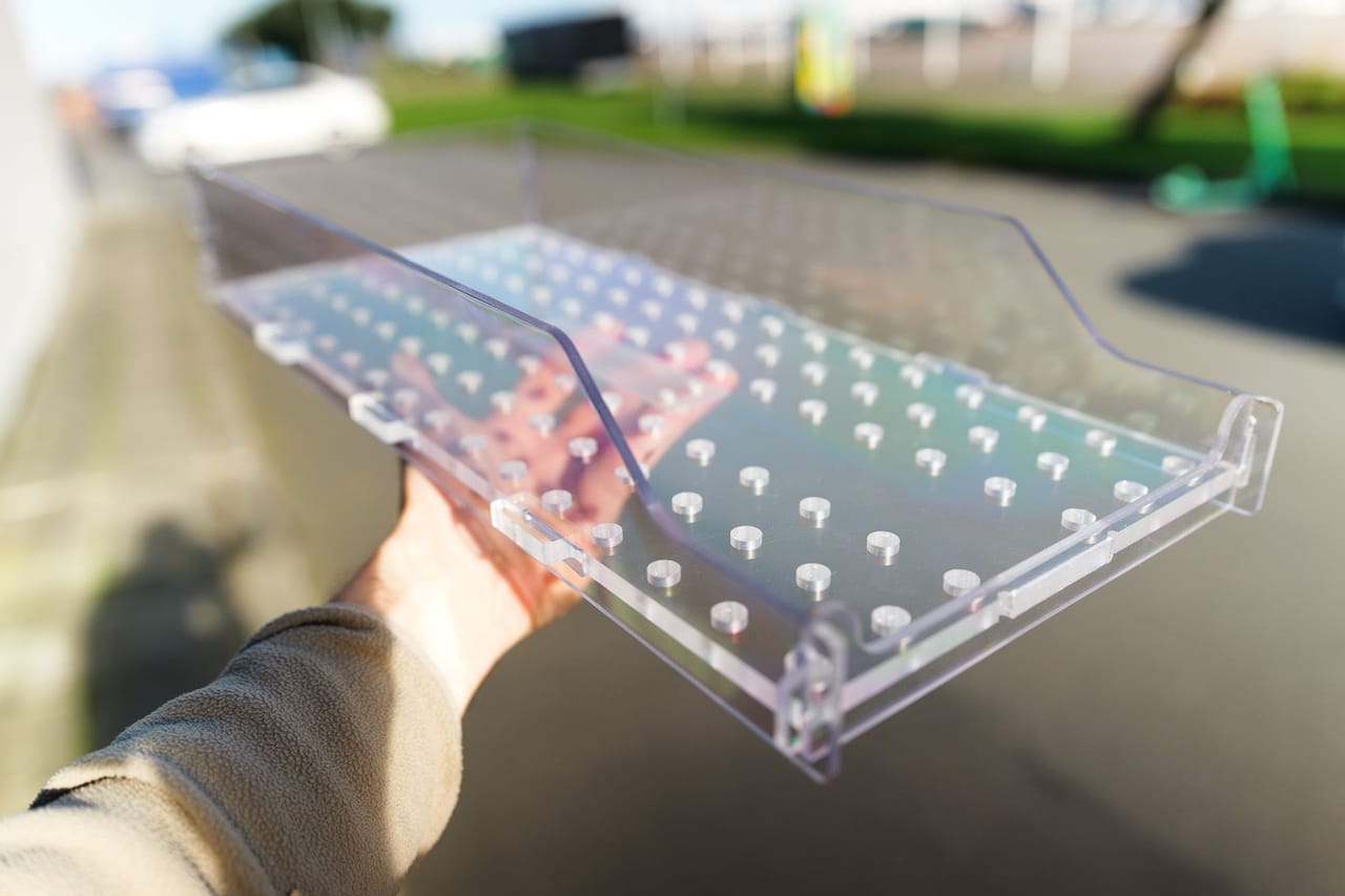 Transparent acrylic tray with a hole pattern, held in a hand outdoors